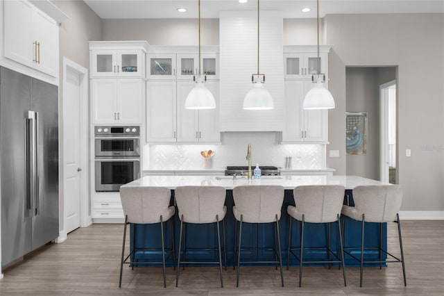 kitchen featuring white cabinets, appliances with stainless steel finishes, a kitchen island with sink, and pendant lighting