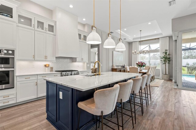 8209 Redonda Loop, Lakewood Ranch, FL 34202 - kitchen featuring a raised ceiling, light wood finished floors, appliances with stainless steel finishes, a kitchen island with sink, and visible vents