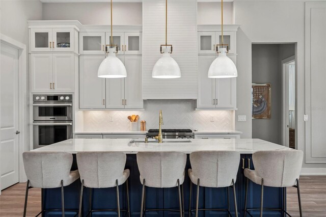 8209 Redonda Loop, Lakewood Ranch, FL 34202 - kitchen featuring pendant lighting, double oven, tasteful backsplash, wood finished floors, and white cabinetry
