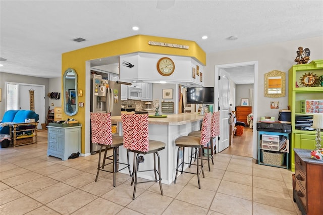 kitchen featuring light tile patterned flooring, a breakfast bar area, white cabinetry, stainless steel appliances, and backsplash