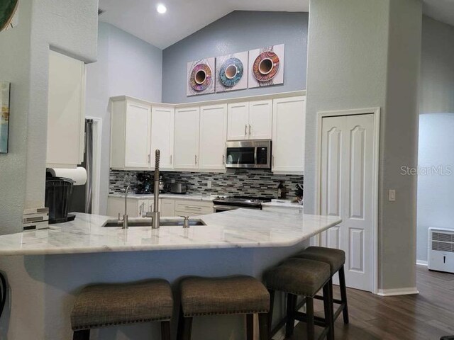 kitchen with light stone counters, kitchen peninsula, appliances with stainless steel finishes, and white cabinetry