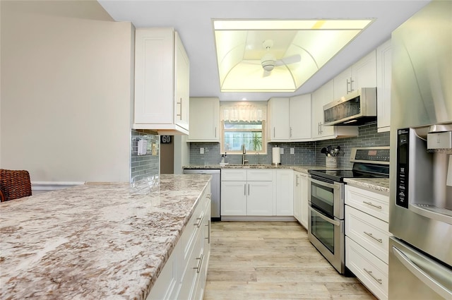 kitchen featuring sink, white cabinets, light wood-type flooring, appliances with stainless steel finishes, and light stone counters