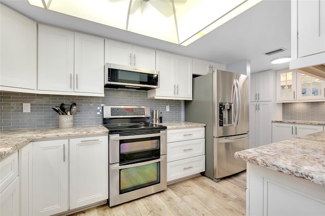 kitchen with appliances with stainless steel finishes, decorative backsplash, white cabinetry, and light wood-type flooring