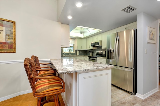 kitchen with a kitchen breakfast bar, light stone countertops, stainless steel appliances, and light wood-type flooring