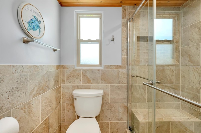 bathroom with toilet, a shower with shower door, and tile walls