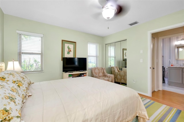 bedroom featuring light hardwood / wood-style flooring, a closet, ensuite bathroom, and ceiling fan