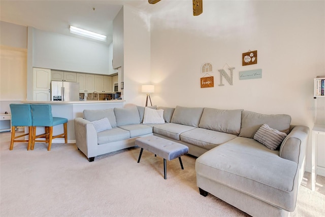 living room featuring a towering ceiling, ceiling fan, light colored carpet, and sink