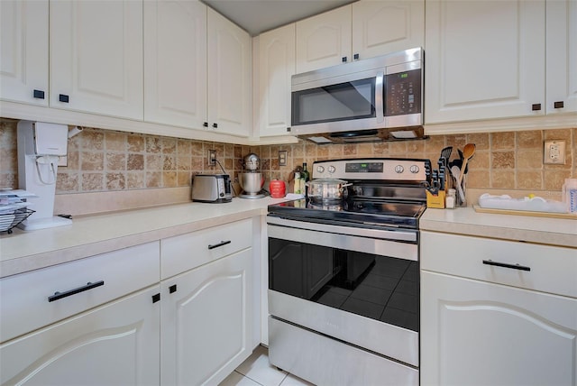 kitchen featuring stainless steel appliances, white cabinets, light tile patterned floors, and backsplash