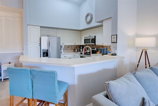 kitchen featuring appliances with stainless steel finishes, a towering ceiling, backsplash, kitchen peninsula, and a kitchen bar