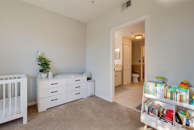 bedroom featuring a crib, connected bathroom, and light colored carpet