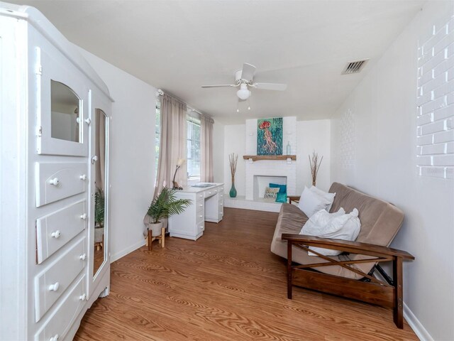 sitting room featuring light wood-type flooring, ceiling fan, and a brick fireplace