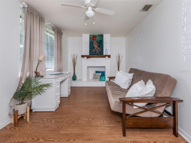 living room with light hardwood / wood-style flooring, a brick fireplace, and ceiling fan