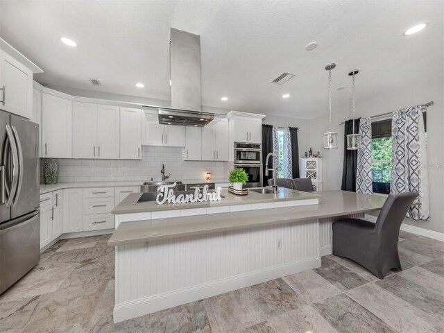 kitchen featuring an island with sink, white cabinets, island exhaust hood, decorative backsplash, and appliances with stainless steel finishes