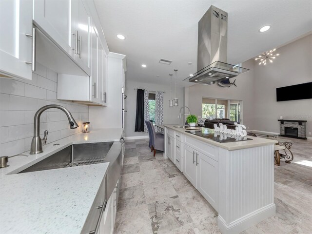 kitchen featuring light stone counters, a stone fireplace, island exhaust hood, and white cabinetry