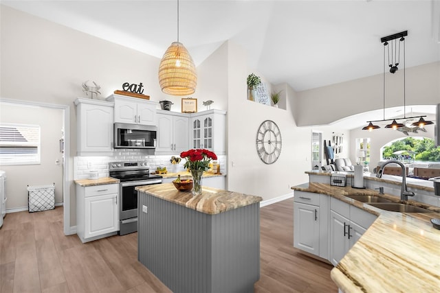 kitchen with sink, decorative light fixtures, stainless steel appliances, a center island, and light hardwood / wood-style floors