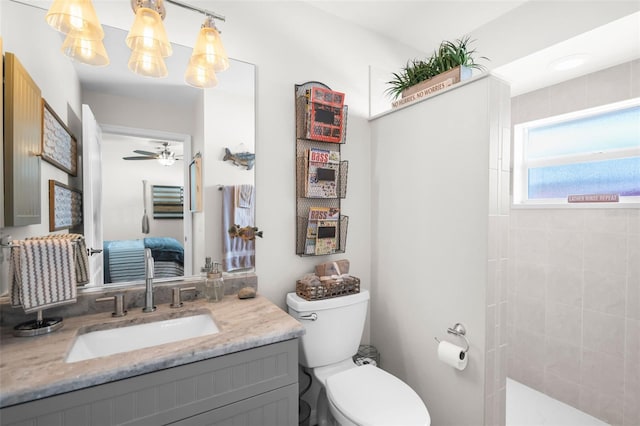 bathroom with tiled shower, ceiling fan, vanity, and toilet