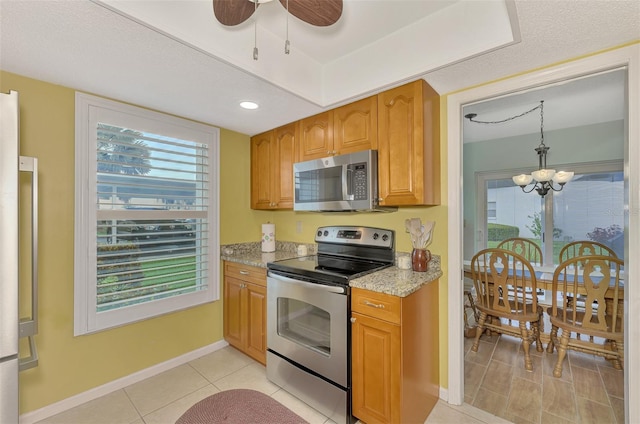 kitchen with pendant lighting, light stone countertops, light tile patterned floors, stainless steel appliances, and ceiling fan with notable chandelier