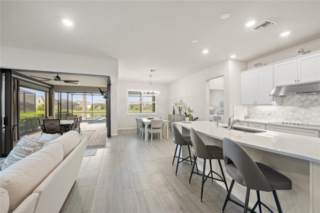 kitchen with a breakfast bar, sink, ceiling fan with notable chandelier, white cabinets, and decorative light fixtures