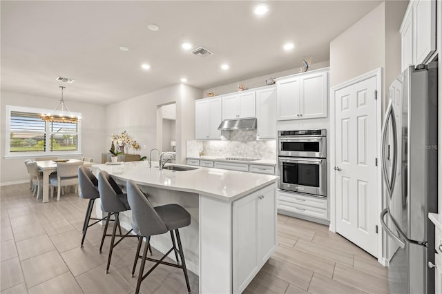 kitchen featuring sink, an island with sink, white cabinets, stainless steel appliances, and decorative light fixtures