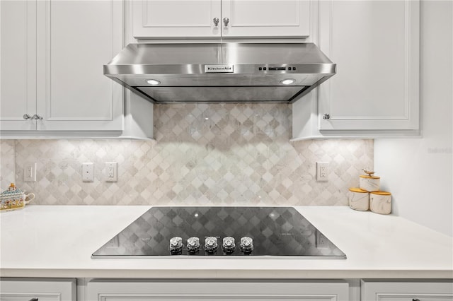 kitchen featuring backsplash, black electric stovetop, wall chimney exhaust hood, and white cabinetry