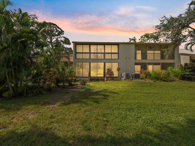 back house at dusk with a balcony, a lawn, and central air condition unit