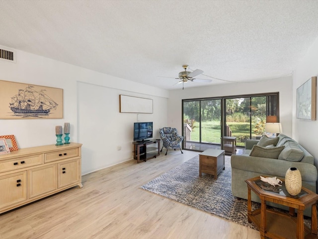 living room featuring light hardwood / wood-style floors, ceiling fan, and a textured ceiling