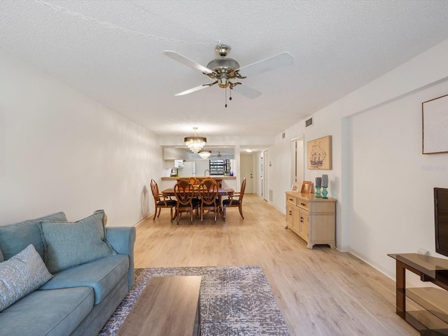 living room featuring light wood-type flooring, ceiling fan with notable chandelier, and a textured ceiling