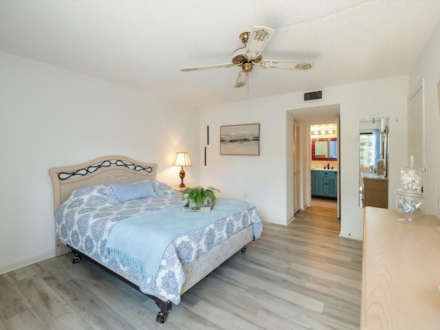 bedroom featuring ceiling fan, a textured ceiling, ensuite bath, and light hardwood / wood-style floors