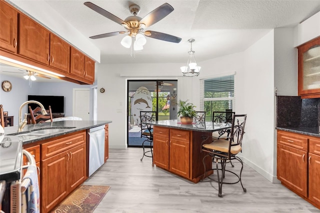 kitchen featuring dark stone counters, light wood-type flooring, dishwasher, a breakfast bar area, and ceiling fan with notable chandelier