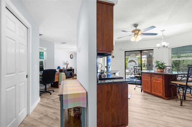 kitchen featuring light wood-type flooring, a textured ceiling, decorative light fixtures, a kitchen breakfast bar, and ceiling fan with notable chandelier