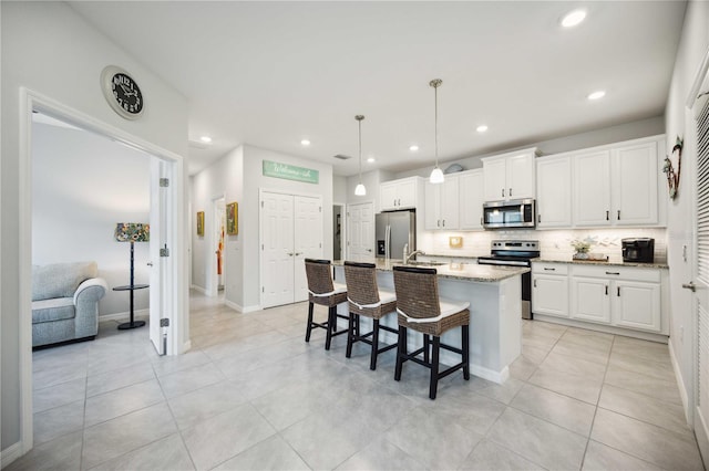 kitchen with white cabinets, an island with sink, tasteful backsplash, stainless steel appliances, and light stone countertops