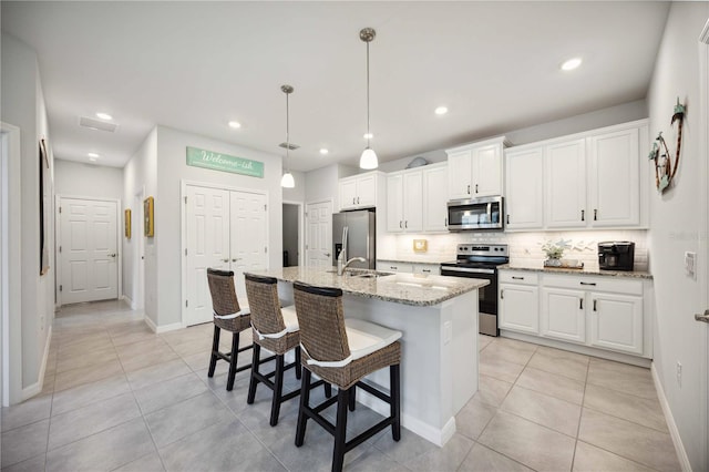 kitchen featuring a center island with sink, backsplash, white cabinetry, stainless steel appliances, and light stone countertops