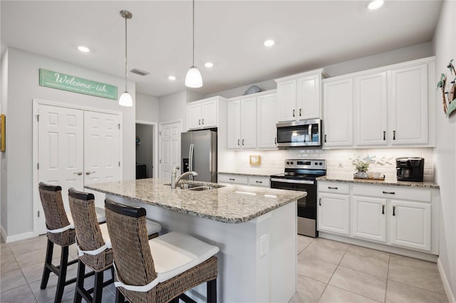 kitchen featuring appliances with stainless steel finishes, hanging light fixtures, an island with sink, white cabinets, and sink