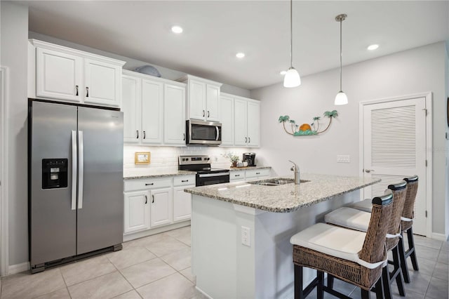 kitchen featuring pendant lighting, a kitchen island with sink, white cabinets, appliances with stainless steel finishes, and light stone countertops