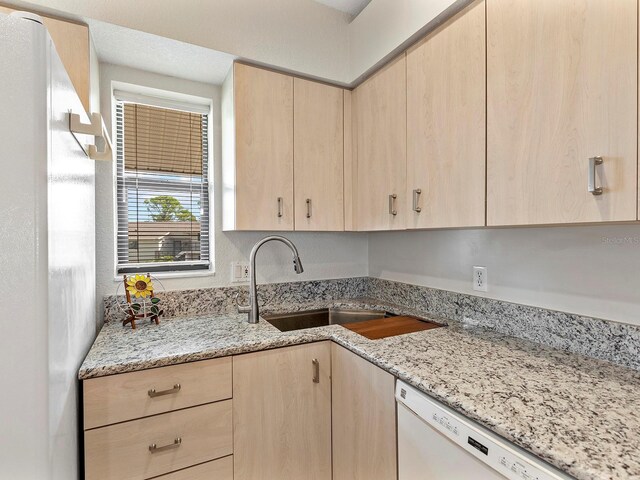 kitchen featuring dishwasher, light brown cabinetry, sink, and light stone counters