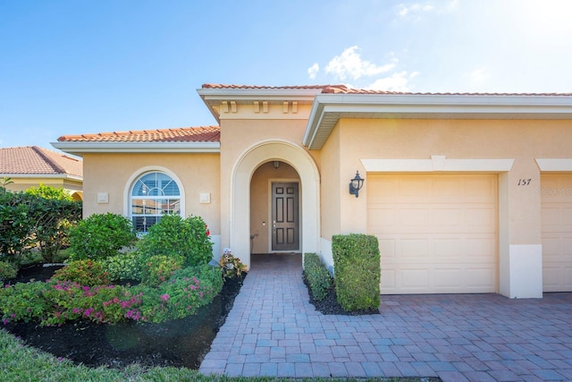 entrance to property with stucco siding, a tile roof, an attached garage, and driveway