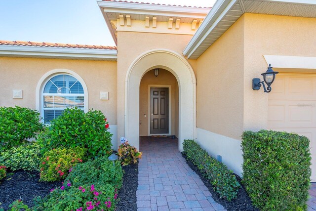 doorway to property featuring a tiled roof, stucco siding, and an attached garage