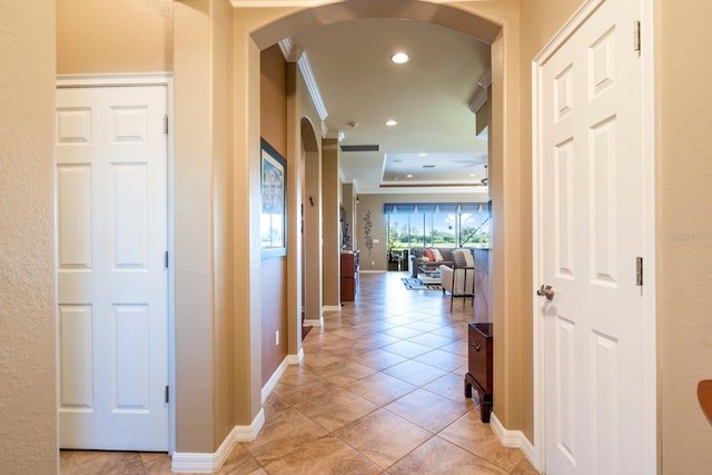 hall with a raised ceiling, light tile patterned floors, baseboards, arched walkways, and recessed lighting