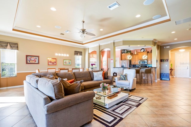 tiled living room with ceiling fan with notable chandelier, a raised ceiling, and ornamental molding