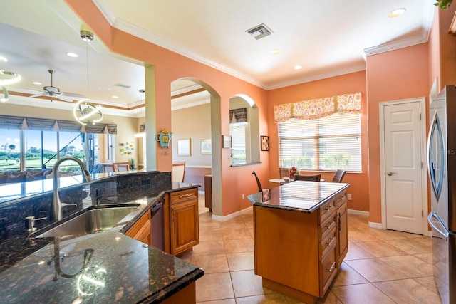 kitchen with a sink, arched walkways, visible vents, freestanding refrigerator, and brown cabinetry