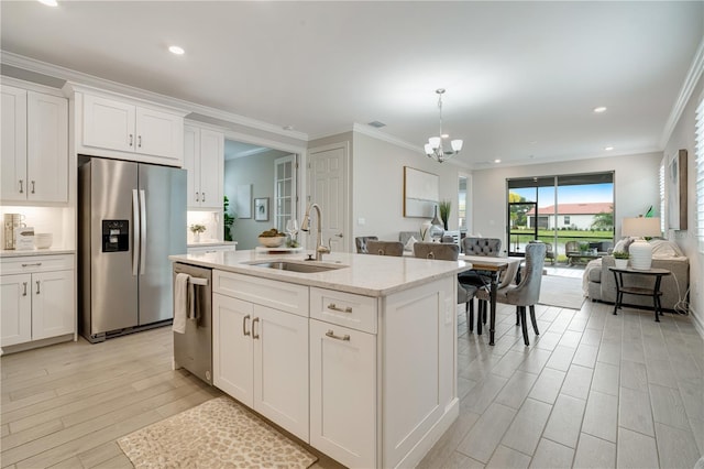 kitchen with sink, a kitchen island with sink, white cabinetry, appliances with stainless steel finishes, and crown molding