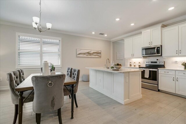 kitchen with white cabinets, pendant lighting, a kitchen island with sink, a chandelier, and stainless steel appliances