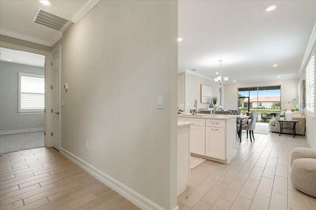 hallway featuring ornamental molding, an inviting chandelier, light hardwood / wood-style floors, and a healthy amount of sunlight