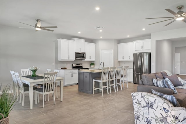 kitchen featuring ceiling fan, white cabinets, an island with sink, and appliances with stainless steel finishes