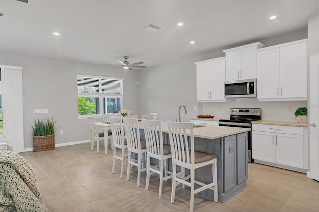 kitchen with ceiling fan, white cabinets, a kitchen island with sink, stainless steel appliances, and a kitchen bar