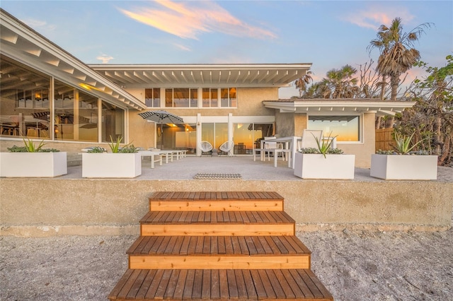 back house at dusk featuring a patio