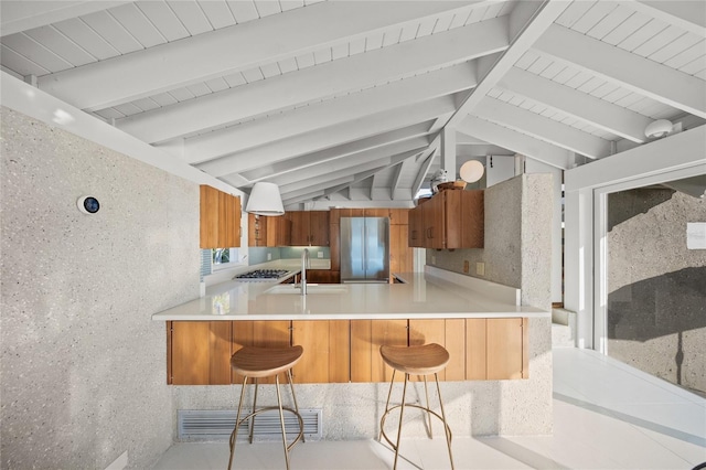 kitchen with sink, vaulted ceiling with beams, stainless steel fridge, a kitchen bar, and kitchen peninsula