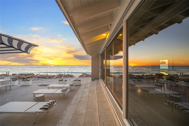 balcony at dusk with a water view and a view of the beach