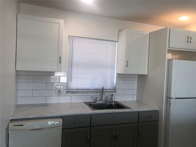 kitchen with tasteful backsplash, white cabinets, white appliances, light stone countertops, and sink