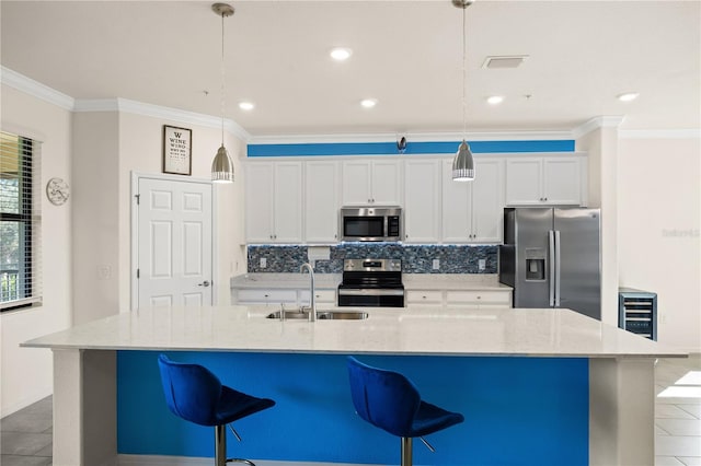 kitchen featuring appliances with stainless steel finishes, an island with sink, white cabinets, pendant lighting, and sink